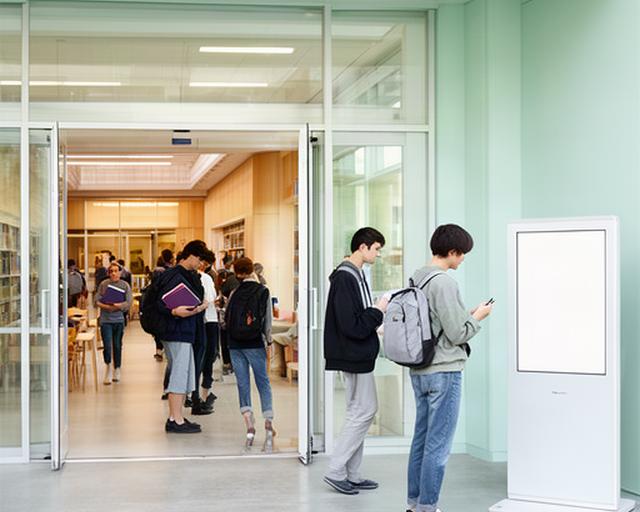 試験期間の大学図書館入口で学生が案内表示を確認している様子